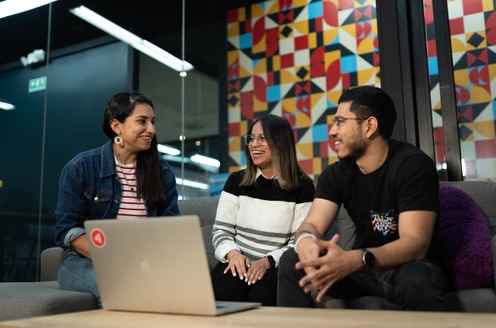 Three individuals seated on a couch, engaged with a laptop, sharing ideas and collaborating in a comfortable setting.