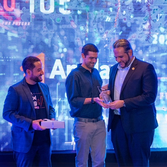 Three men proudly holding an award together at a formal event, celebrating their achievement