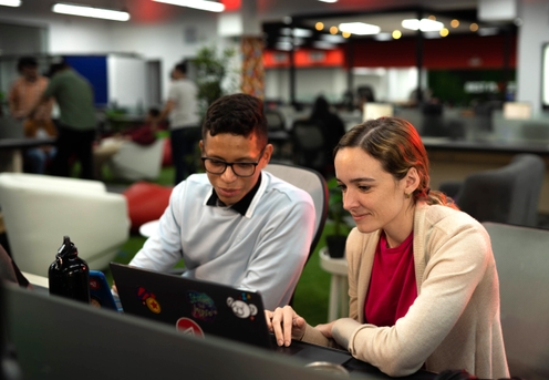 Two Applaudo employees collaborating on laptops in a modern office environment.