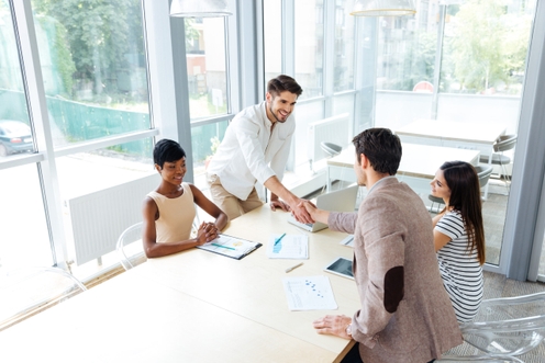 A group of people at a table, with one man shaking hands with another, symbolizing collaboration and agreement.