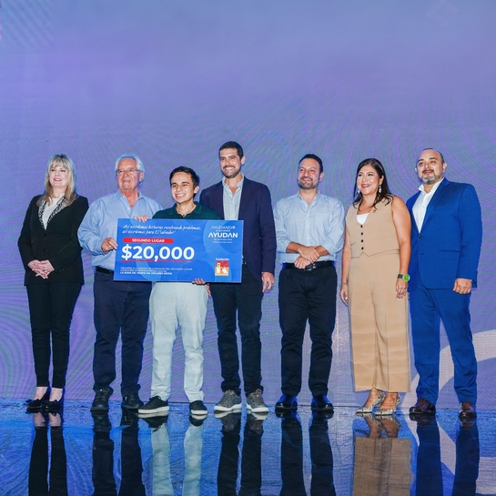 A diverse group of individuals proudly stands in front of a large check, celebrating their achievement together