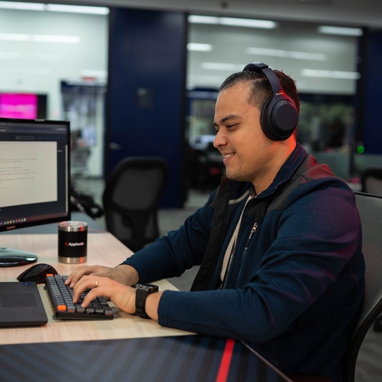 A software developer manager wearing headphones sits at a desk, focused on his computer screen, immersed in his work.