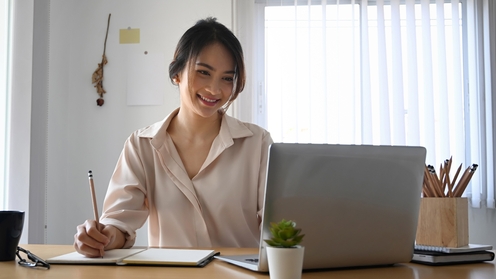 Female operations professional taking notes and smiling to a laptop screen in an office