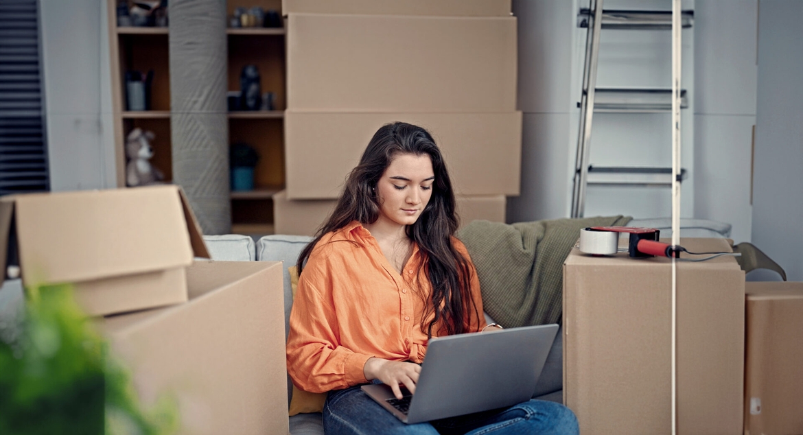 A real estate agent sitting comfortably on a couch, focused on her laptop while working or browsing online.