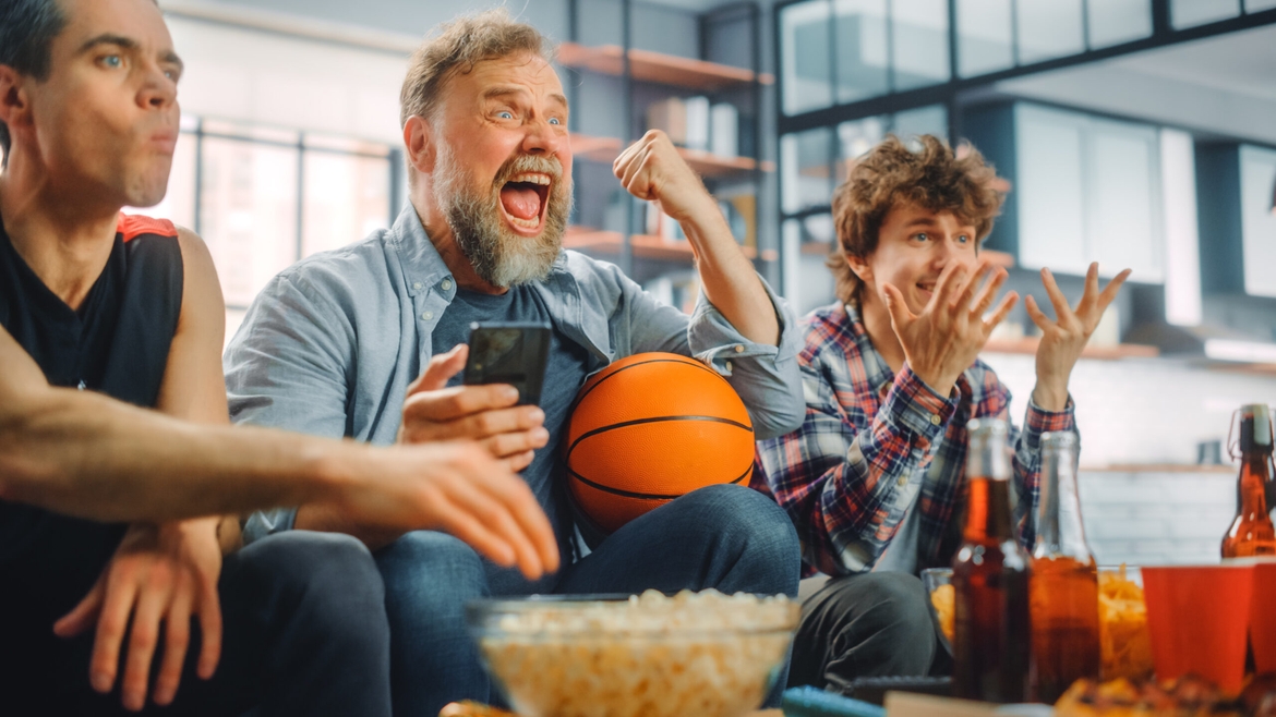 Fans Sitting on Couch Watch Basketball Game on TV, Use Smartphone App for Checking Score, Bet, Statistics, Celebrate when Team Wins Championship.